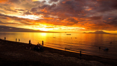 Silhouette people at beach against sky during sunset