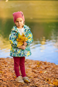 Portrait of girl holding leaves standing by lakeshore