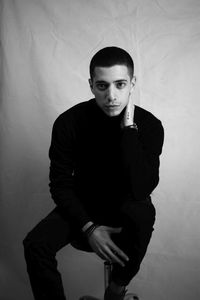 Portrait of young man sitting against wall