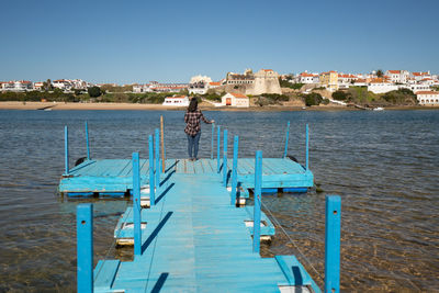 Rear view of woman standing on pier by lake against cityscape