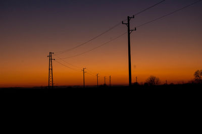 Silhouette electricity pylons against orange sky