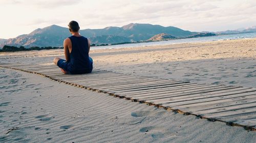 Rear view of man sitting on boardwalk at beach