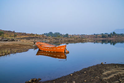 Fishing boat moored in lake against sky