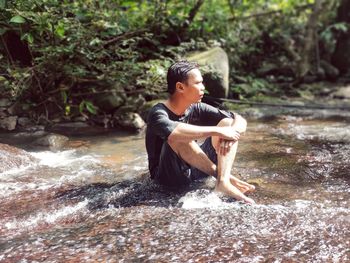 A person in black is sitting on a rocky shallow stream