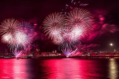 Firework display over illuminated city against sky at night