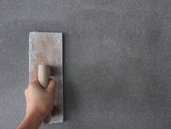 Close-up of worker using scrapper on gray wall at construction site