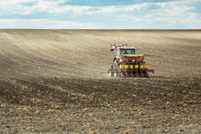 Agricultural tractor fertilizes in a plowed field, horizon and clouds on the sky