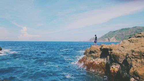 Man standing on rock by sea against sky