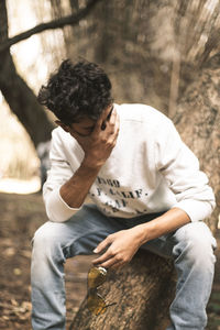 Young man sitting on tree trunk