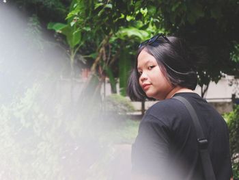 Portrait of beautiful young woman standing against plants