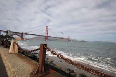 View of suspension bridge over sea against cloudy sky