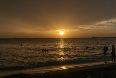 Silhouette people on beach against sky during sunset