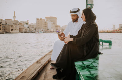 Couple using smart phone while sitting in boat on river during sunset