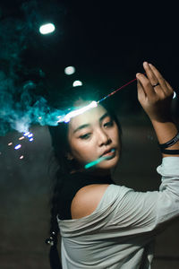 Young woman holding illuminated sparkler at night