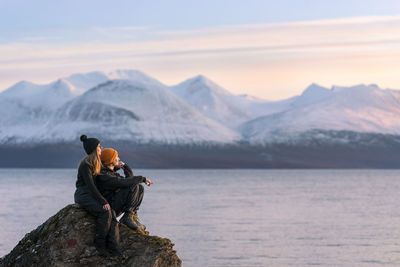 People on rock by lake against sky