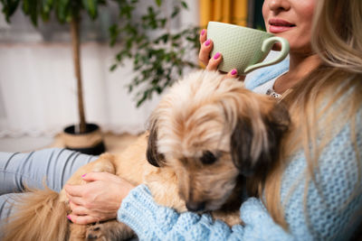 The girl is drinking coffee and the dog is cuddling with her.