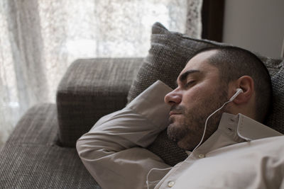 Close-up of man listening music while lying sofa sitting at home