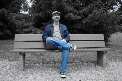 Portrait of young man sitting on bench in park