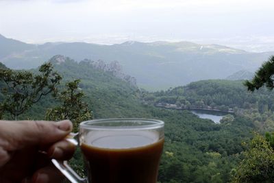 Midsection of person holding drink against mountains