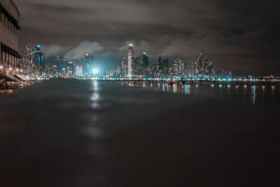Illuminated city by sea against sky at night