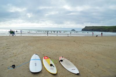 View of sandy beach with surfboards and sea against sky