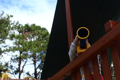 Low angle view of girl playing with telescope on railing at balcony