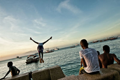 Rear view of boy jumping in sea against sky