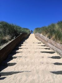 Low angle view of man walking on sand against clear blue sky