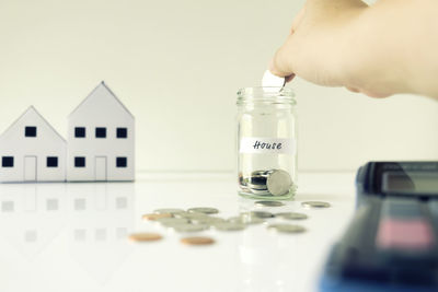 Cropped hand of man putting coin in jar on table