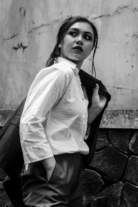 Portrait of a young woman standing against wall