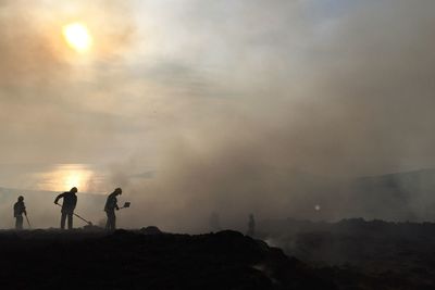 Silhouette men working on land against sky during sunset