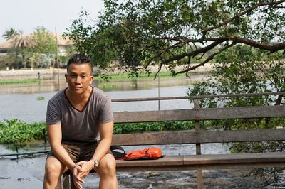 Portrait of man sitting on bench against lake