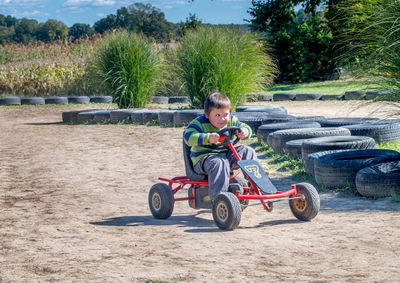 Happy boy races around a dirt track in a little pedal car