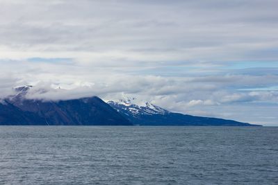 Scenic view of sea by snowcapped mountains against sky