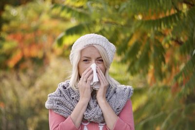 Portrait of woman holding hat against plants during winter