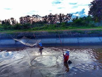 Men fishing in water against sky