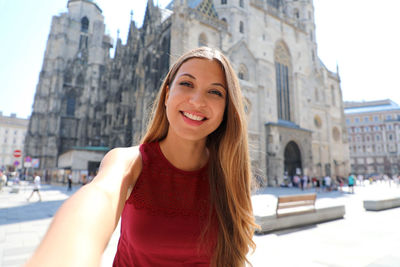 Portrait of smiling young woman against building in city