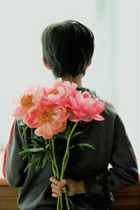 Rear view of boy holding pink flowers at home