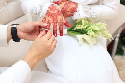 Midsection of groom putting ring in bride finger sitting on sofa during wedding