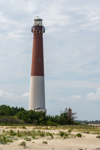 Lighthouse on field by building against sky