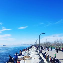 People on sea shore against blue sky