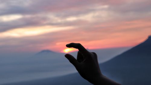 Silhouette person hand against sky during sunset