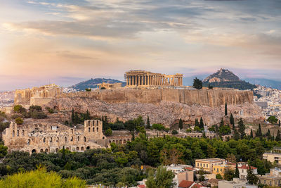 Distant view of old ruins in city against cloudy sky during sunset