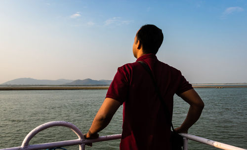 Rear view of man looking at sea against sky