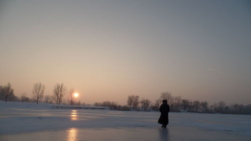 Silhouette of man on snowy field against sky during sunset