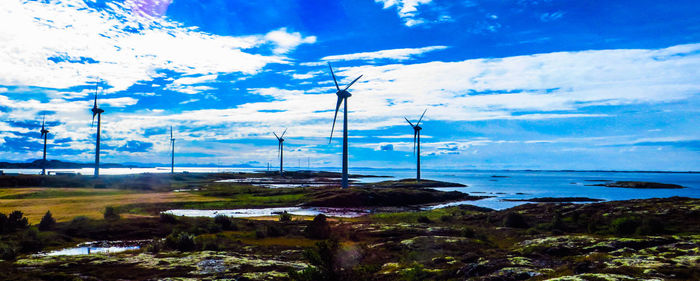 Windmills by sea against blue sky