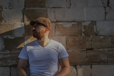 Young man looking away against brick wall