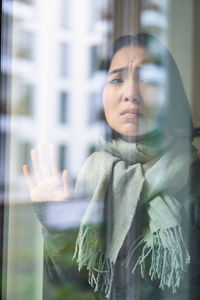 Portrait of young woman standing against window