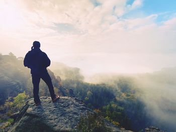 Rear view of man standing on mountain against sky