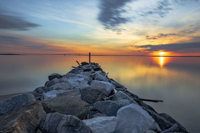 Rocks by sea against sky during sunset